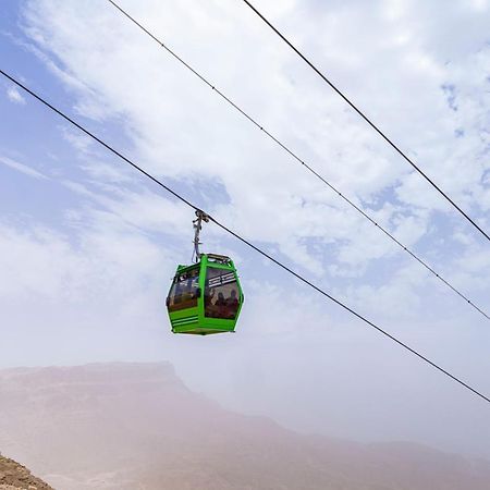 Tolip Resort El Galala Majestic Ain Soukhna Exteriér fotografie The photo shows a green cable car suspended in the air, traveling along overhead cables. The backdrop features a hazy landscape, likely mountainous or elevated terrain, with a cloudy sky. The scene suggests a scenic transportation method, possibly us