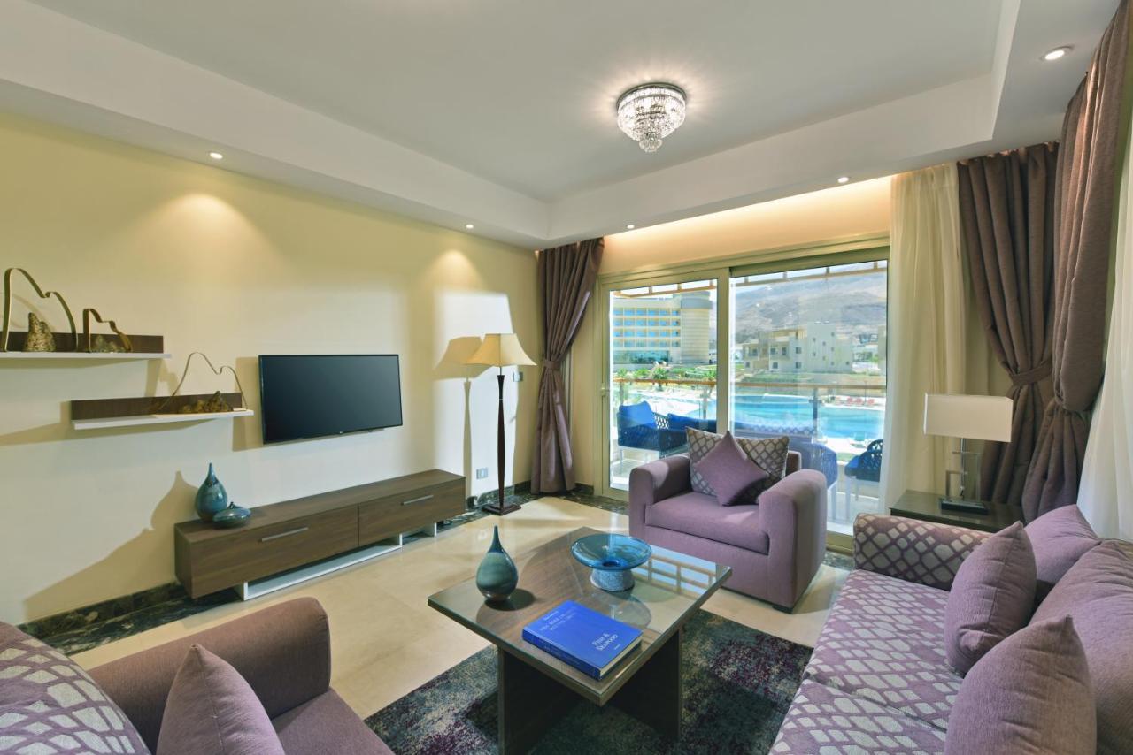 Tolip Resort El Galala Majestic Ain Soukhna Exteriér fotografie The photo shows a modern living room that features a stylish and cozy design. There are two purple sofas with decorative cushions arranged around a coffee table. The coffee table has a blue book and a decorative item on it. A flat-screen TV is mounte