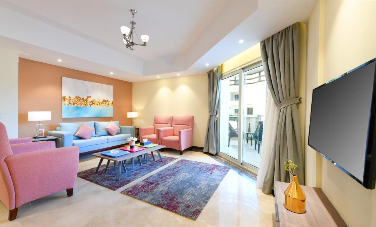 Tolip Resort El Galala Majestic Ain Soukhna Pokoj fotografie The photo shows a modern living room that features a cozy and stylish design. There is a light blue sofa adorned with pastel pink cushions, accompanied by two pink armchairs. A coffee table sits in front, placed on a colorful area rug that adds warmt