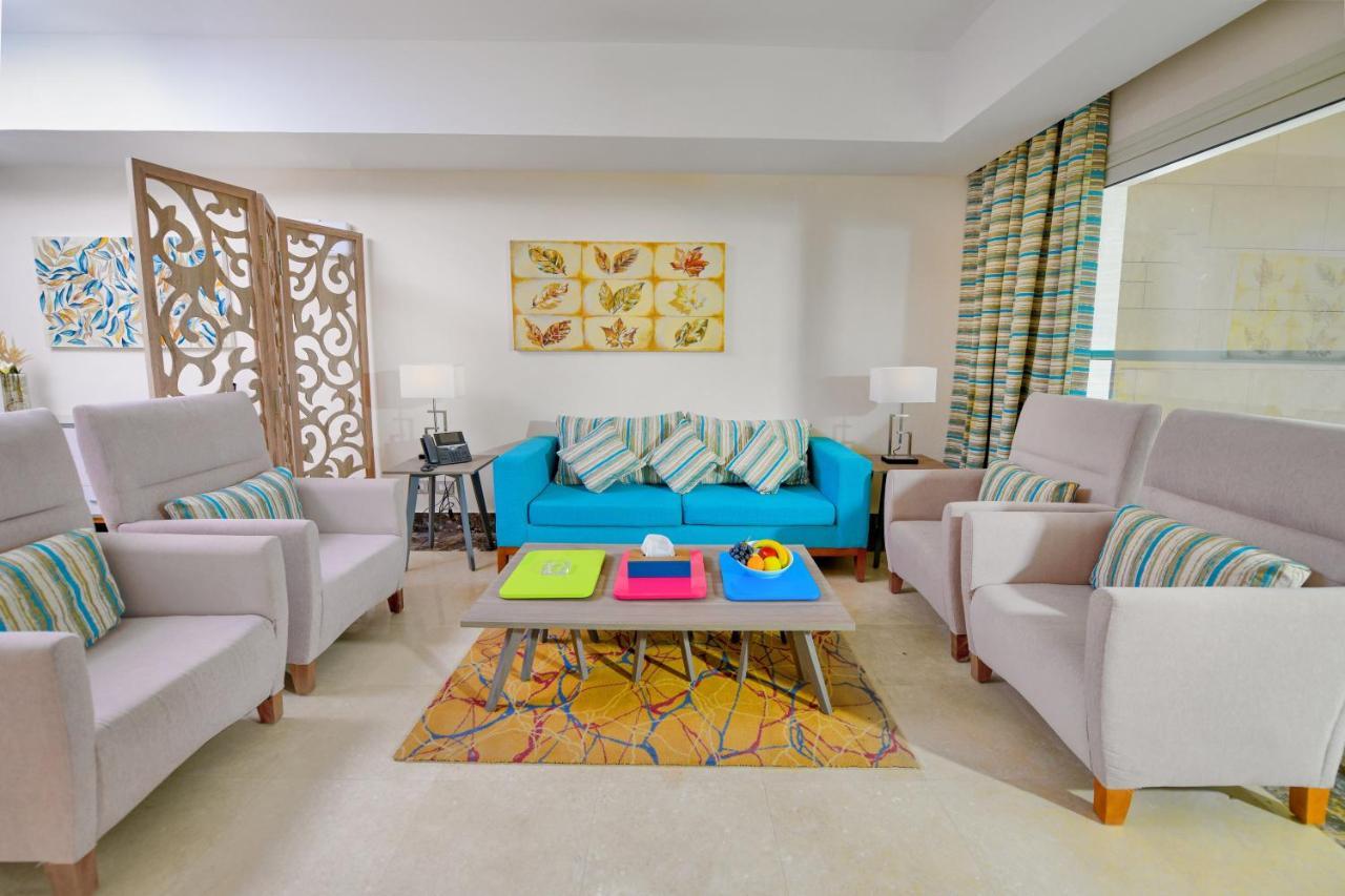 Tolip Resort El Galala Majestic Ain Soukhna Exteriér fotografie The photo shows a stylish and colorful living room. It features a bright blue sofa with patterned cushions, complemented by two light gray armchairs. In front of the sofa, there's a wooden coffee table with vibrant trays in pink, green, and yellow. A
