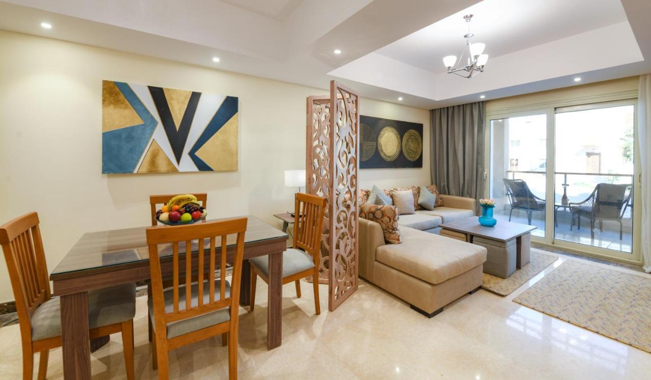 Tolip Resort El Galala Majestic Ain Soukhna Exteriér fotografie The photo shows a modern and stylish interior of a living space. It features a seating area with a plush sofa and decorative cushions, complemented by a wooden coffee table. There is a dining table with wooden chairs nearby. 

On the walls, there are