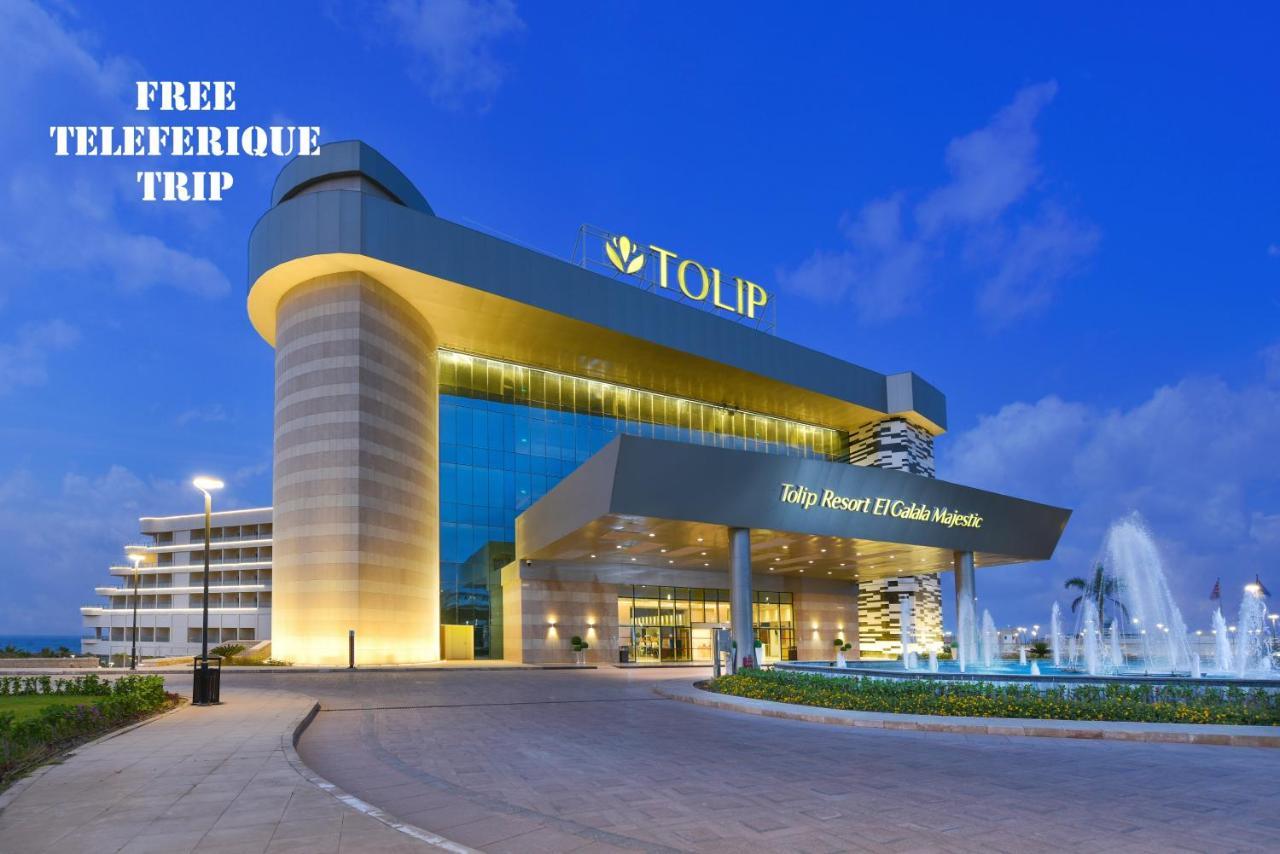 Tolip Resort El Galala Majestic Ain Soukhna Exteriér fotografie The photo shows a modern hotel building named "Tolip Resort & Spa," featuring a sleek architectural design with large glass windows. The hotel is illuminated against a twilight sky, showcasing its prominent signage. In the foreground, there is a well