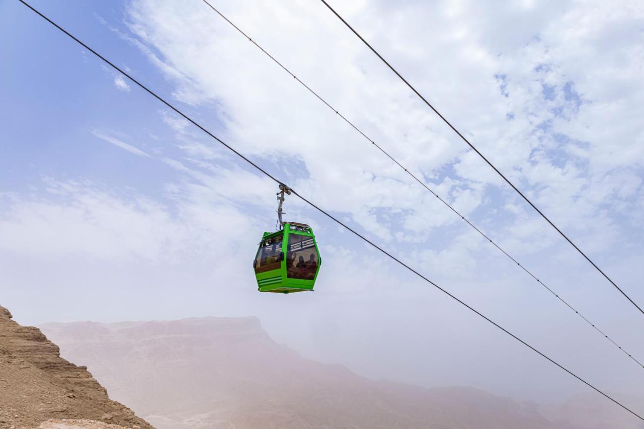 Tolip Resort El Galala Majestic Ain Soukhna Exteriér fotografie The photo shows a green cable car suspended in the air, traveling along overhead cables. The backdrop features a hazy landscape, likely mountainous or elevated terrain, with a cloudy sky. The scene suggests a scenic transportation method, possibly us
