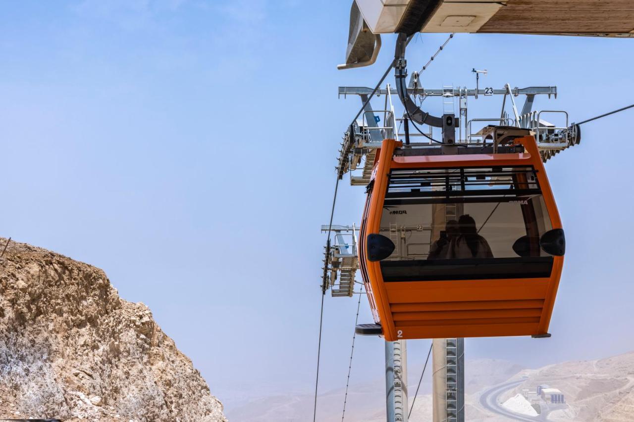 Tolip Resort El Galala Majestic Ain Soukhna Exteriér fotografie The photo shows an orange gondola or cable car hanging on a cable system. The gondola appears to be suspended in the air above a rocky landscape, with a clear sky in the background. There are supporting cables and structures visible, indicating that 