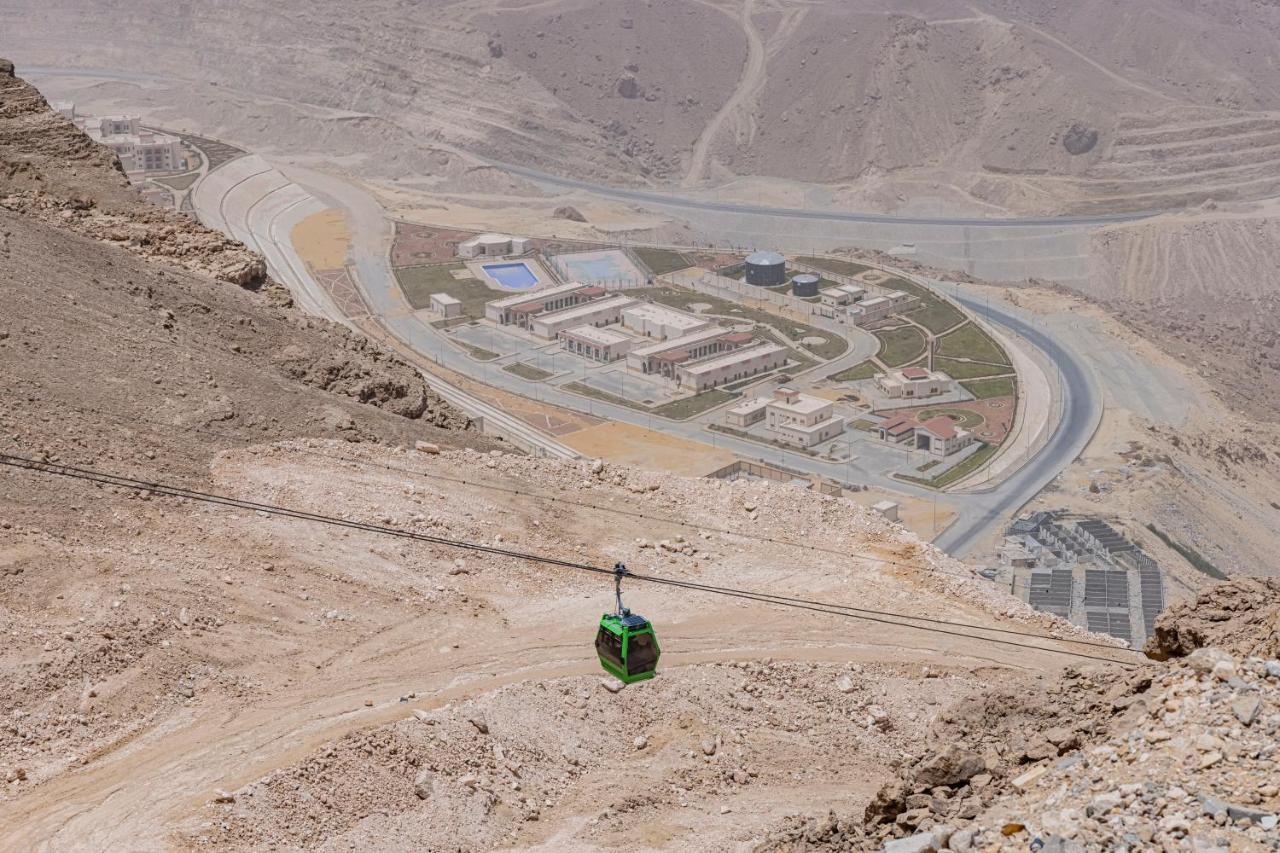 Tolip Resort El Galala Majestic Ain Soukhna Exteriér fotografie The photo shows a mountainous landscape with a steep, dry terrain. In the foreground, there is a green cable car or gondola traveling along a cable. Below, a complex of buildings and roads can be seen, likely part of a resort or recreational area. Th