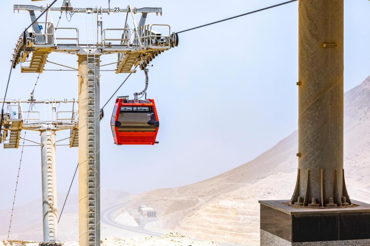Tolip Resort El Galala Majestic Ain Soukhna Exteriér fotografie The photo shows a cable car system with a single red gondola suspended mid-air. It appears to be part of a larger cable car infrastructure, with metal pylons supporting the cables above. The background features a hazy landscape, likely characterized 