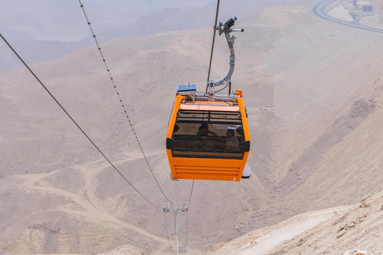Tolip Resort El Galala Majestic Ain Soukhna Exteriér fotografie The photo shows an orange cable car suspended in the air, traveling along a set of cables. It appears to be located in a mountainous or hilly area, with rugged terrain and dry, rocky landscapes visible below. The background features slopes that seem 