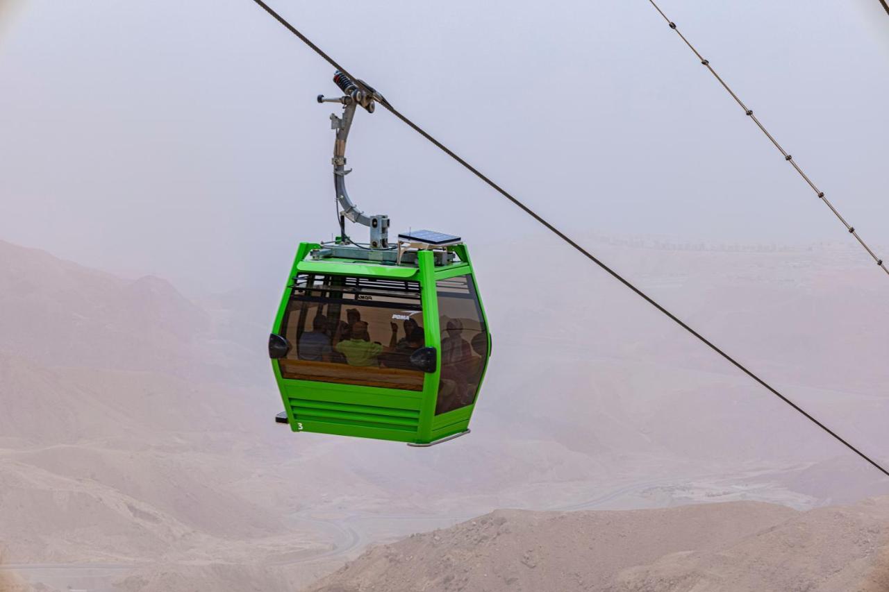 Tolip Resort El Galala Majestic Ain Soukhna Exteriér fotografie The photo shows a green cable car suspended in the air, moving along a wire. The cable car appears to be traversing a mountainous landscape, which looks rocky and arid. The surrounding environment is somewhat foggy or hazy, suggesting limited visibil
