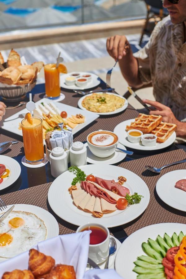 Tolip Resort El Galala Majestic Ain Soukhna Exteriér fotografie The photo shows a breakfast spread laid out on a table. There are several plates with a variety of food items, including:

1. **Sliced Cold Cuts**: A plate featuring various cold meats, accompanied by garnishes like cherry tomatoes and lettuce.
2. **