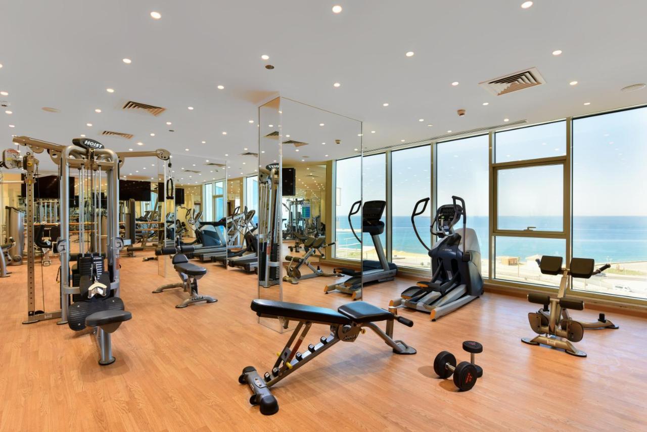 Tolip Resort El Galala Majestic Ain Soukhna Exteriér fotografie The photo shows a modern gym interior with a variety of fitness equipment. There are cardio machines like treadmills and ellipticals, along with strength training equipment such as free weights and benches. The gym features large windows that offer a