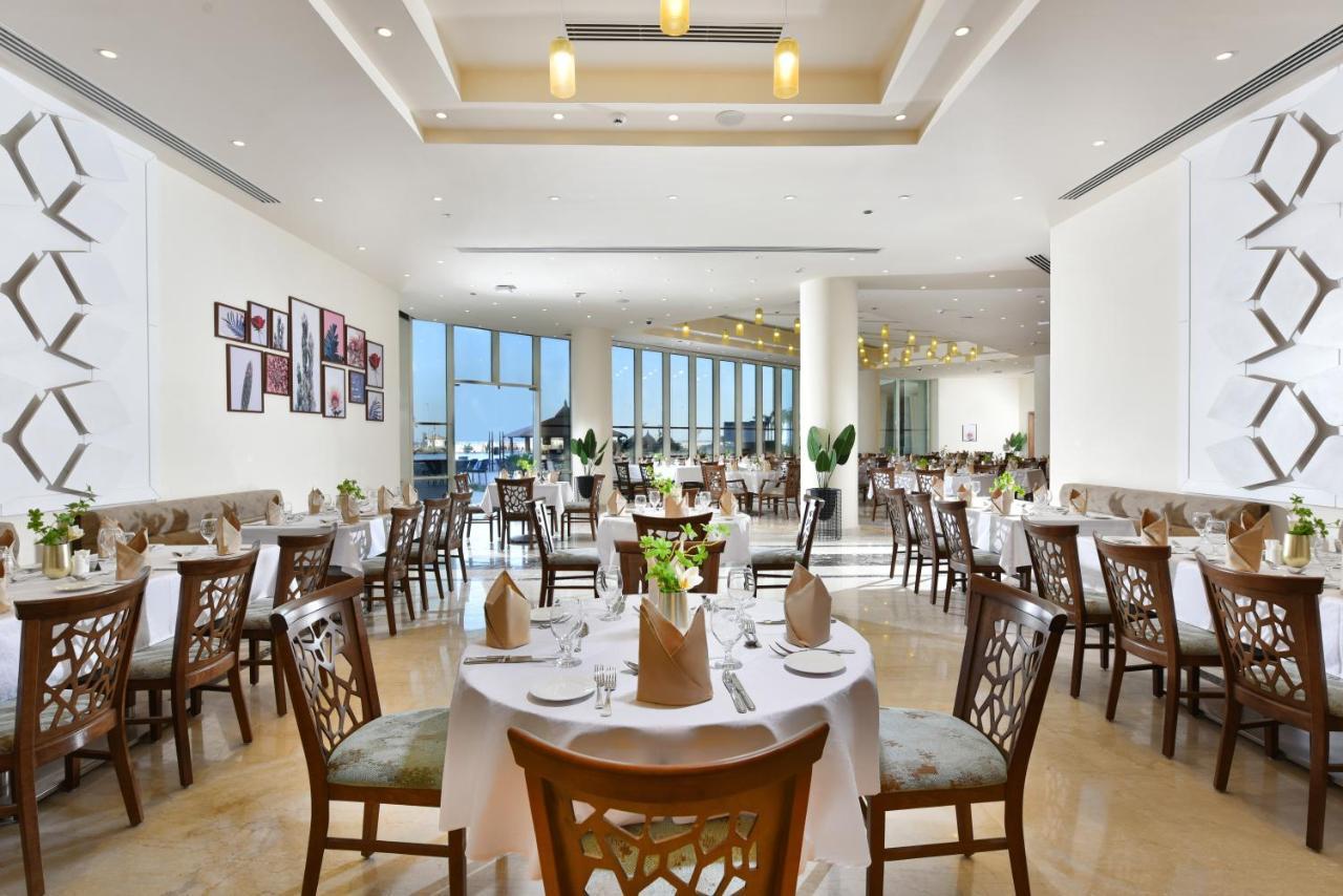Tolip Resort El Galala Majestic Ain Soukhna Exteriér fotografie The photo displays a spacious and elegantly designed restaurant interior. It features numerous tables set for dining, with white tablecloths, neatly folded napkins, and decorative centerpieces of flowers. The seating consists of wooden chairs that co