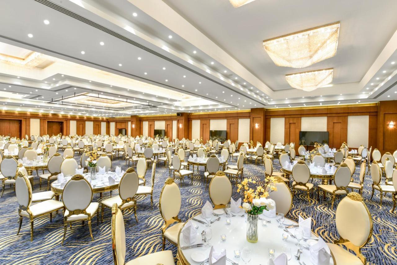 Tolip Resort El Galala Majestic Ain Soukhna Exteriér fotografie The photo shows a spacious and elegantly decorated banquet hall. The room features numerous round dining tables, each set with white tablecloths and adorned with decorative centerpieces, likely flowers. The chairs surrounding the tables have a luxuri
